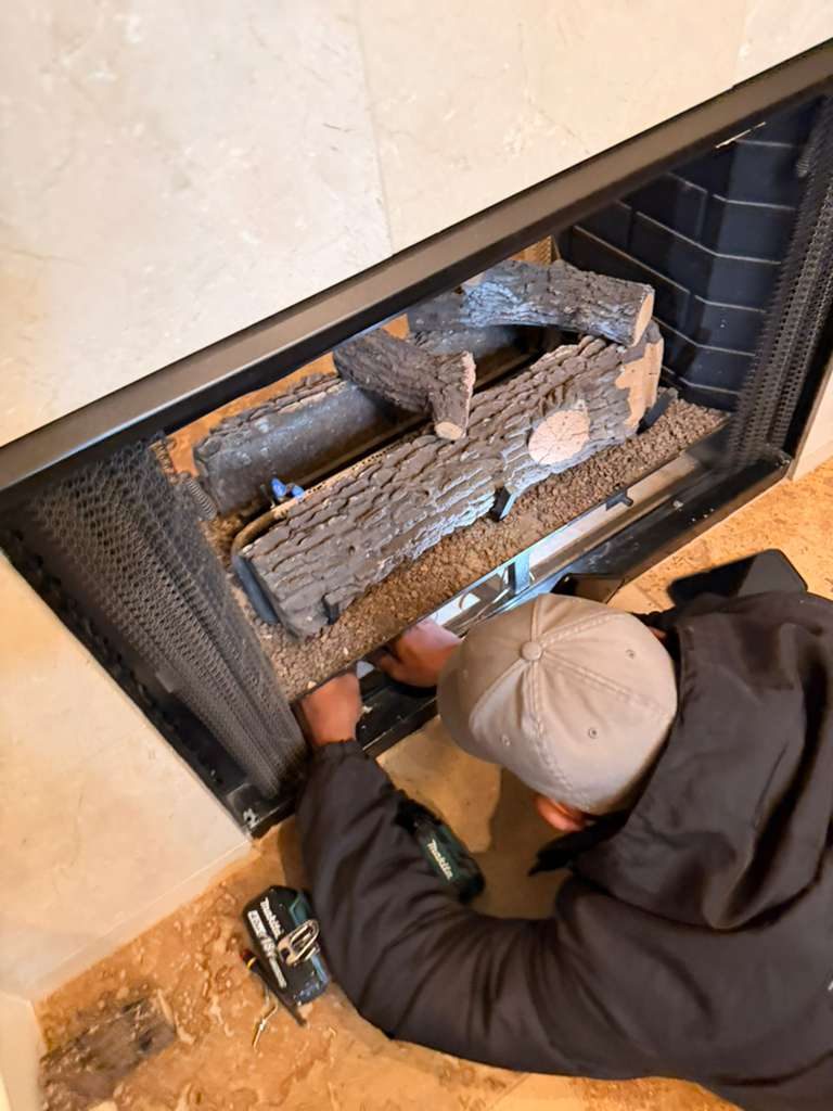 Ember Chimney & Fireplace technician repairing the burner and gas log set of a gas fireplace in a Dallas-Fort Worth home