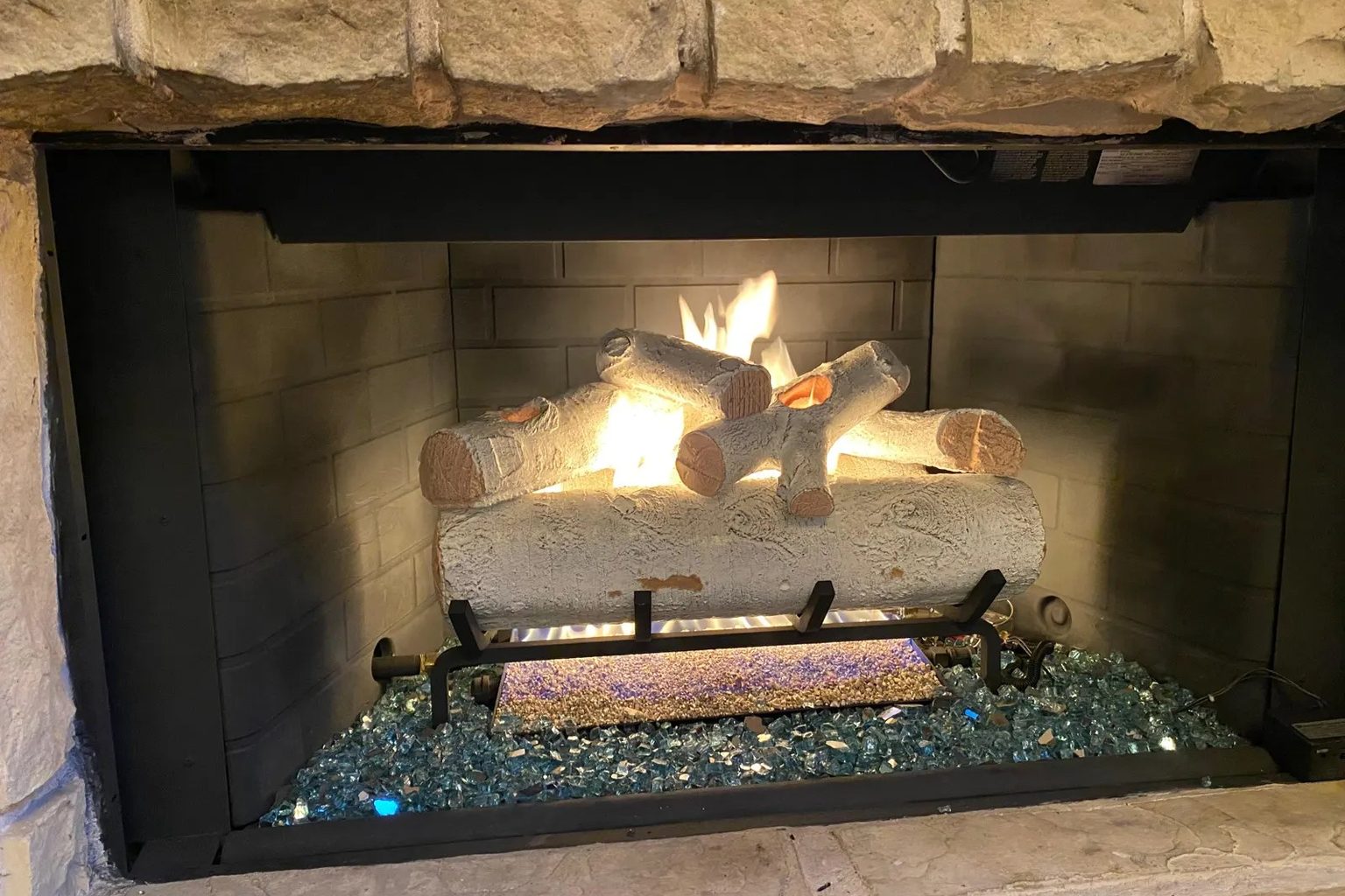 Gas log set installed and lit in a fireplace by Ember Chimney & Fireplace